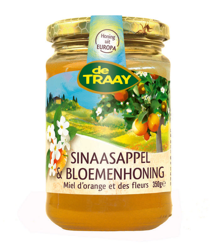 Jar of de Traay Sinaasappel and bloemenhoning honey with fresh orange slices and flower decorations on a wooden surface