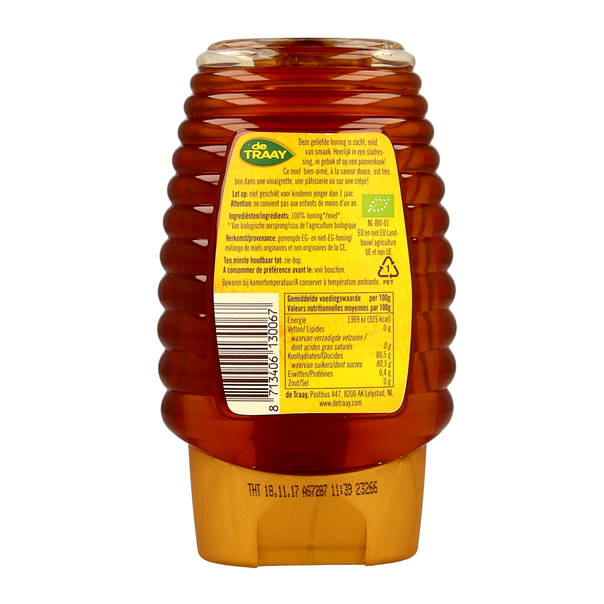 Jar of de Traay organic flower honey in a clear glass bottle, with a gold lid and honey visible through the glass.
