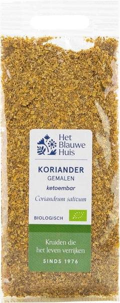 Ground organic coriander from Het Blauwe Huis, 25g, in a clear jar with fresh green coriander leaves beside it.